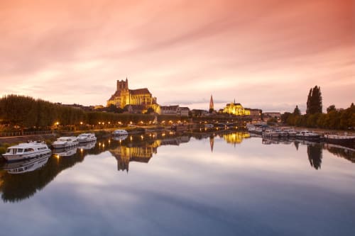 Petite ville fluviale de Bellechaume au crépuscule, cathédrale illuminée, bateaux et reflets dans les eaux calmes