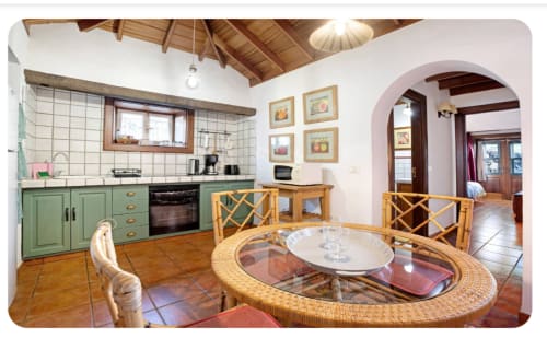 Cocina y comedor abiertos en La Palma entre viñas, con muebles verdes, mesa redonda de mimbre y tonos terracota