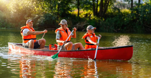 Três pessoas remando uma canoa vermelha nas águas tranquilas do rio perto da Casa da Serração, Rio Caldo Portugal