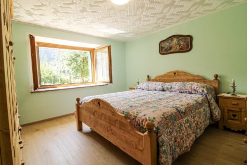 Helles grünes Schlafzimmer mit Holzbett und Bergblick vom Fenster in der Wohnung Da Beppinesca, Santo Stefano di Cadore