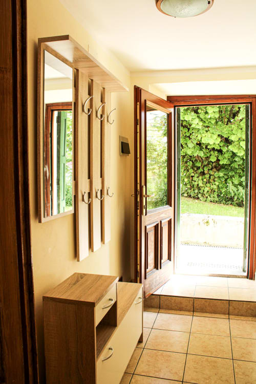 Eingangsbereich mit eingebautem Holzbanken und Spiegel, offene Tür zum Garten mit üppigem Grün, Fliesenbelag in Santo Stefano di