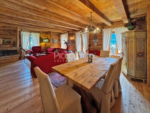Lussuoso appartamento alpino in legno a Cortina d'Ampezzo con tavolo da pranzo rustico, sedute in velluto rosso e vista sulle montagne