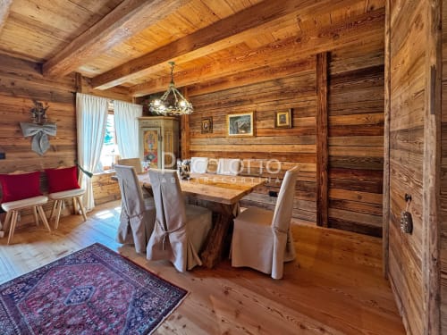 Sala da pranzo in rustica baita a Cortina d'Ampezzo con travi in legno, tavolo formale e vista sulle montagne.