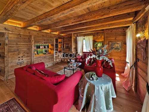 Lussuoso salotto in chalet di legno a Cortina d'Ampezzo con divano rosso, camino e vista sulle montagne
