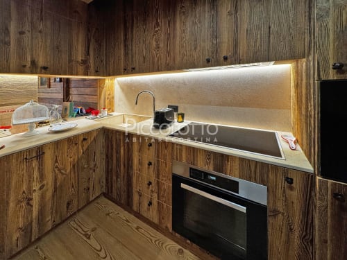 Cucina moderna in appartamento alpino a Cortina d'Ampezzo con mobili in legno, lavello in acciaio inox e elettrodomestici incassati