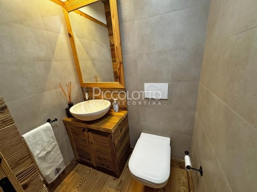Bagno moderno nell'appartamento Alpen Maison a Cortina d'Ampezzo, con vanity in legno, lavabo rotondo, specchio, wc e piastrelle grigie