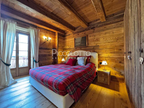 Accogliente camera da letto in legno a Cortina d'Ampezzo con coperta scozzese rossa, travi a vista, balconate e vista sulle montagne