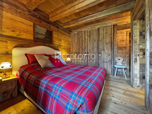 Camera da letto in legno accogliente a Cortina d'Ampezzo con biancheria scozzese rossa, travi rustiche e arredamento in stile alpino