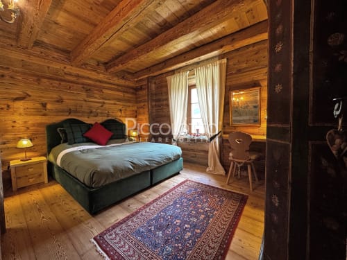 Camera da letto alpina accogliente a Cortina d'Ampezzo con letto, camino, viste montane e arredamento tradizionale