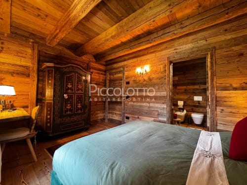 Camera da letto in rustica baita a Cortina d'Ampezzo con travi in legno, letto, guardaroba decorato e bagno ensuite