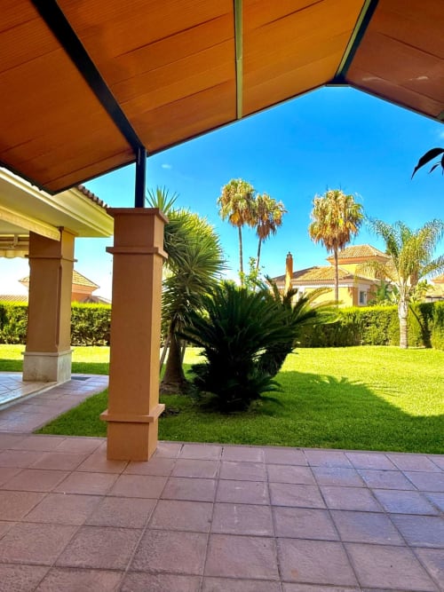 Patio del BH Marbella con pilares de terracota, palmeras, jardín impecable y vista al mar bajo cielo azul despejado