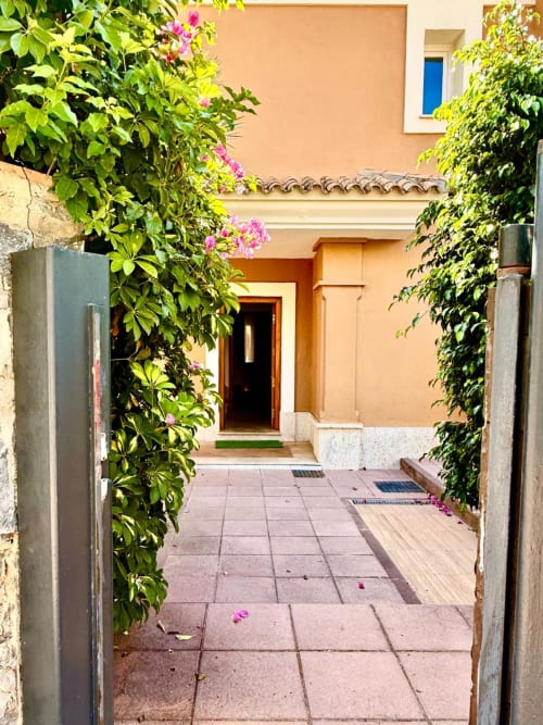 Encantador acceso al patio de BH Marbella con flores rosadas, muros cubiertos de hiedra y fachada de terracota