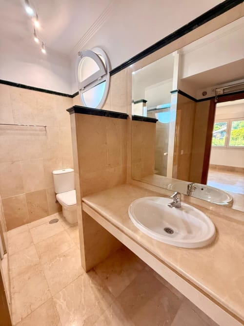 Baño moderno en BH Marbella con lavamanos, espejo, inodoro y ducha tipo walk-in con cabina de vidrio