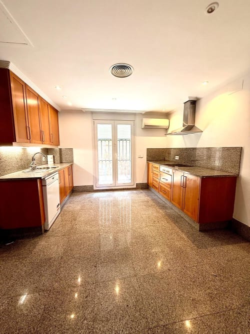 Amplia cocina moderna en BH Marbella con muebles de madera, encimeras de granito, electrodomésticos de acero inoxidable y piso pulido