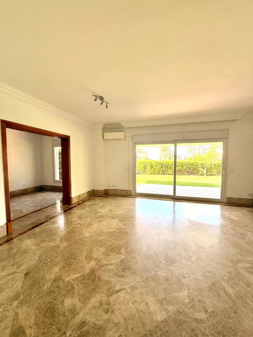 Amplio salón en BH Marbella con suelos de mármol, espejo de marco rojo, puertas correderas de cristal hacia terraza, y