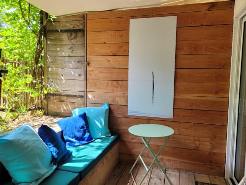 Terrasse privée du Lodge du Cap Ferret avec coussins bleus, tableau blanc, petite table et mur en bois dans un jardin