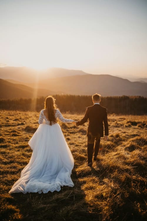 Casal recém-casado de mãos dadas em campo ao pôr do sol dourado com montanhas, Herdade da Côrte, Tavira