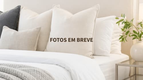 Quarto elegante em Herdade da Côrte com almofadas brancas e creme macias, roupa de cama impecável e plantas em vaso na mesinha de cabeceira