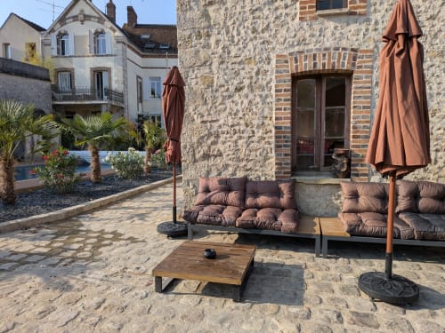 Patio extérieur du Domaine de La Poule Noire avec murs en pierre, sièges confortables, parasols et vue sur le jardin dans l'annonce Airbnb