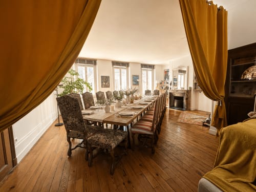 Élégante salle à manger du Domaine de La Poule Noire avec table longue, chaises motifs et rideaux dorés donnant sur le jardin