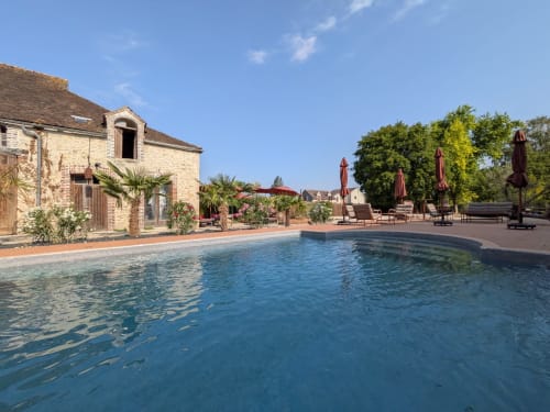 Piscine privée du Domaine de La Poule Noire avec bâtisse en pierre, terrasse en terre cuite et vue sur le jardin sous ciel dégagé