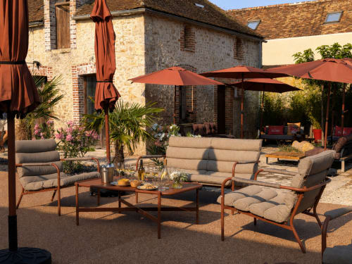 Élégante cour de détente au Domaine de La Poule Noire avec architecture en pierre, parasols en terre cuite et sièges confortables.