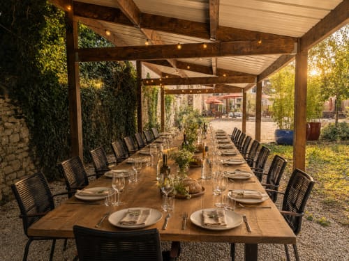 Élégant pavillon de dining extérieur au Domaine de La Poule Noire avec longue table en bois, chaises noires, murs couverts de lierre