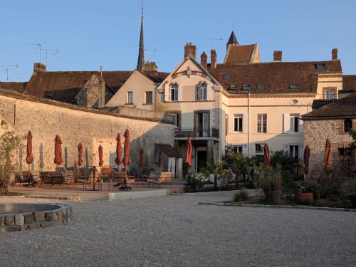 Cour du Domaine de La Poule Noire avec murs en pierre, parasols rouges et architecture française historique
