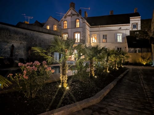 Domaine de La Poule Noire illuminé la nuit, jardin éclairé, palmiers et bâtisse en pierre historique