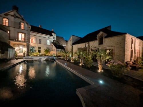 Domaine de La Poule Noire illuminé la nuit avec piscine, terrasse et bâtiments en pierre sous un ciel dégagé