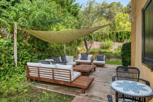 Terraza exterior de la villa Finques Garcia Enrich en Palafrugell con mobiliario de madera, vela de sombra y exuberante jardín