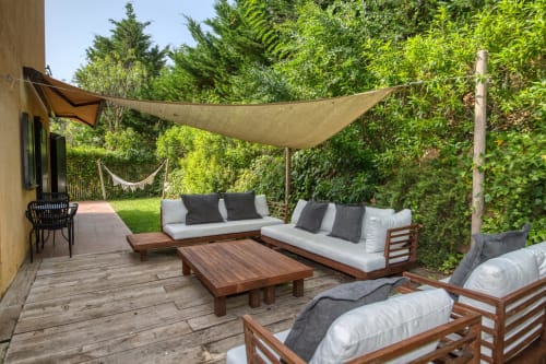 Terraza exterior con muebles de madera para descansar, cojines blancos y toldo en la villa Finques Garcia Enrich en Palafrugell
