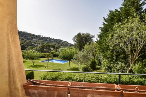 Balcón de terracota con macetas que domina frondosos jardines, piscina y bosque en villa de Palafrugell