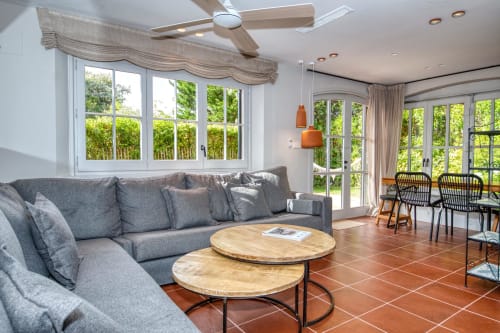 Luminoso salón de villa moderna en Palafrugell con sofá gris, mesas de madera y vistas al jardín por ventanales