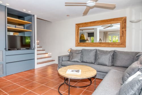 Salón moderno de villa en Palafrugell con sofá gris, espejo de madera, televisión y suelos de barro cocido