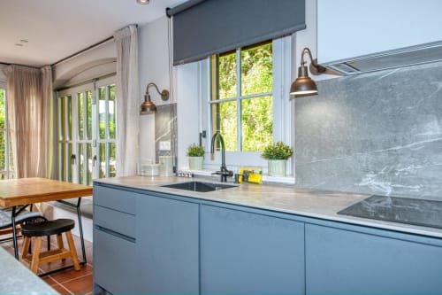 Cocina moderna con gabinetes azules, encimeras de mármol y amplios ventanales con vistas a la vegetación en una villa de Palafrugell.