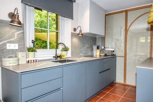Cocina moderna con cajonería azul, encimeras de mármol y amplios ventanales con vistas al jardín de la villa La Pastora