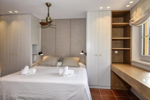 Dormitorio moderno en villa de Palafrugell con armarios empotrados, cabecero tapizado en gris, escritorio de madera y estanterías encastradas