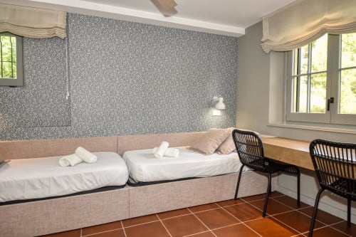 Dormitorio moderno en villa de Palafrugell con camas gemelas, cabecero beige, pared con patrón y sillas negras