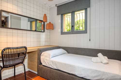 Dormitorio moderno con cama gris, zona de escritorio y amplias ventanas en la villa La Pastora en Llafranc, Palafrugell