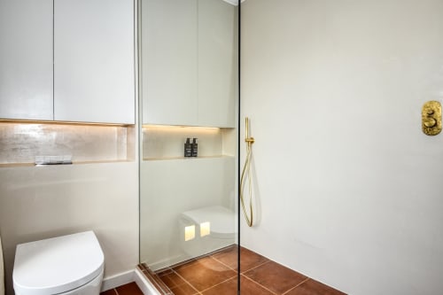 Baño moderno con ducha abierta, inodoro, toallero calefactor y accesorios de latón en la villa La Pastora en Llafranc,
