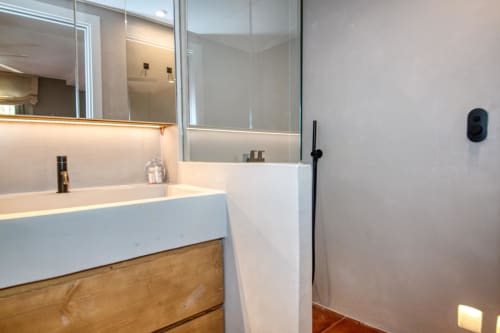 Baño moderno con lavamanos blanco, tocador de madera, espejo iluminado y ducha en la villa La Pastora, Llafranc, Palafrugell