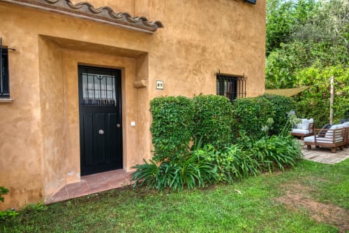 Entrada de villa de terracota con puerta negra, setos podados y jardín en La Pastora, Llafranc
