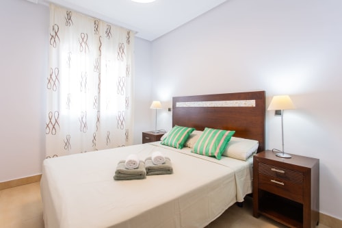Modern bedroom at Haus Holiday Homes with wooden bed, green striped pillows, towels, and patterned curtains