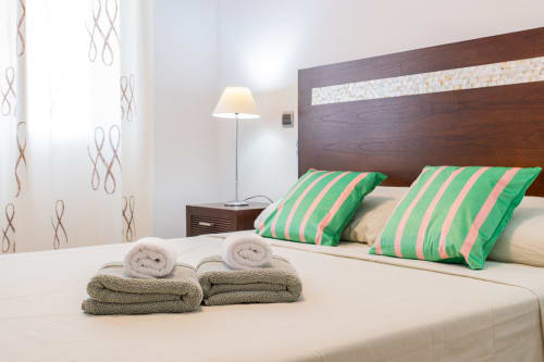 Modern bedroom at Haus Holiday Homes with striped green pillows, rolled towels, and dark wood headboard in San Pedro del