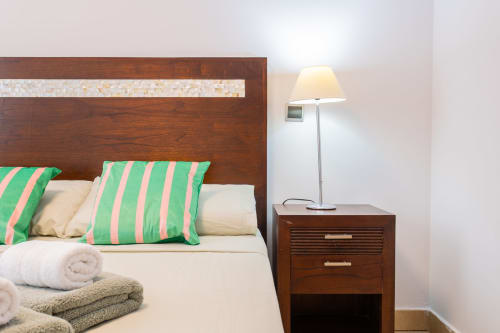Modern bedroom at Haus Holiday Homes with wood headboard, green striped pillows, cream bedding, and bedside lamp in San Pedro