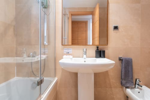 Modern bathroom with pedestal sink, mirror, shower enclosure, and beige tile walls at Haus Holiday Homes apartment in San
