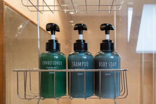 Three bathroom amenity bottles (conditioner, shampoo, body soap) in 300ml sizes displayed on shower shelf at Haus Holiday