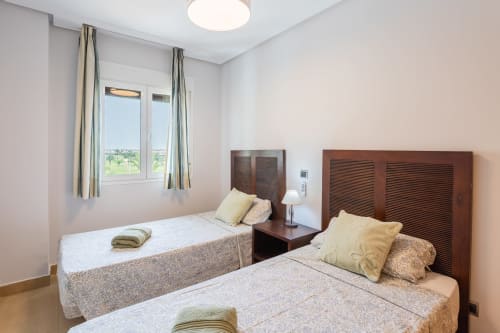 Twin bedroom with wooden headboards, yellow pillows, side table, window with countryside views at Haus Holiday Homes