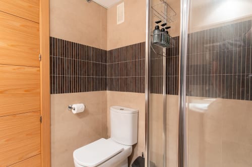 Modern bathroom with black and beige tile walls, toilet, and walk-in shower at Haus Holiday Homes apartment in San Pedro del